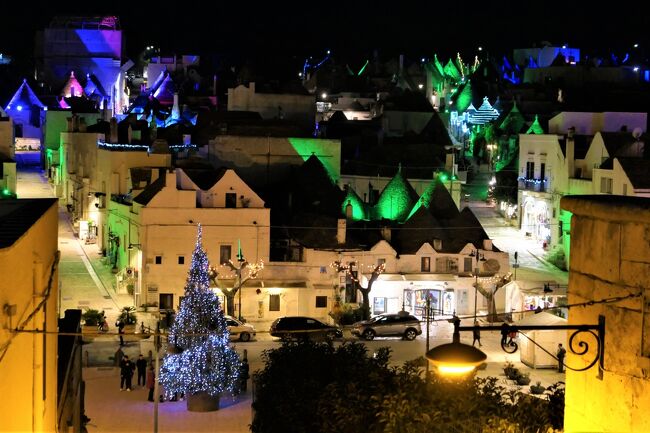 プーリアのクリスマス！2019年12月5日-17日プーリア州に行きました♪クリスマスに彩られた素敵な町、キラキラと輝くクリスマスイルミネーション、可愛い手作りのクリスマスマーケット、美味しい冬のグルメをたっぷりと楽しんできました♪<br /><br />☆Vol.149：第8日目（12月12日）アルベロベッロ（バーリ県）♪<br />今日はオストゥーニから日帰り♪<br />メザーニェ→ブリンディジ→アルベロベッロ。<br />アルベロベッロは6日前の昼間に行っており、<br />今回は夜のイルミネーション鑑賞。<br />2階建ての白いトゥルッロ・ソヴラーノは華やかな色彩のプロジェクションマッピング。<br />次から次へと美しい色合いが現れて幻想的。<br />南へ歩くとお馴染みのアルベロベッロ大聖堂「Basilica Santuario Parrocchia Santi Medici Cosma e Damiano」。<br />その教会前にクリスマスツリーが置かれて華やいだ雰囲気。<br />そこから旧市街へのメインストリート「Corso Vittorio Emanuele」。<br />ショップが連なる繁華街でディスプレイは素晴らしい。<br />クリスマスムードが満載。<br />可愛い雑貨屋さんでショッピング。<br />ポポロ広場では流れ星が美しい。<br />そこから展望台の広場へ行くと、<br />モンテ地区のカラフルなパノラマに感動。<br />青、緑、紫、ピンクとあちこちとライトアップ。<br />冬のアルベロベッロは美しい。<br />ゆったりと歩いて眺めて♪