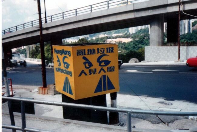 1980年にロンドンに行くときトランジットで<br />数時間滞在したことはあるが、本格的には初香港、<br />というかトランジットは別でアジア自体が初めて。<br />どこか大手の半日市内観光付きの 3泊4日のフリーツアー。<br />結果的には香港が気に入り何度も再訪することになるが、<br />前回は 12月末で意識しなかったが、この時は真夏。<br />夏生まれだが暑さは苦手で 香港(東南アジア)の<br />暑い夏を知らず(というか初めてだし)、<br />塩が残るほど吹き出す汗に辟易し、<br />以後は夏に香港に行くことは避けている。<br /><br />写真はバスの中から見つけたものだが<br />亂抛垃圾人見人憎 (Hong Kong Is Watching) とある。<br />これだけでは外国人には意味は分からないが、<br />中国の Wiki によると…<br />在1981年,香港政府以「亂抛垃圾、人見人憎」<br />作為八十年代初期清潔香港運動的宣傳口號,<br />並配以一雙怒目而視的雙眼作為清潔香港運動的標誌,<br />宣傳的手法亦相當具阻嚇性,措辭亦相當嚴厲。<br /><br />要するに 81年から政府が "清潔な香港" を目指す<br />クリーン・キャンペーンの標語として使ったもので<br />ポイ捨ては許さない! 見張ってるぞ! と<br />怖い顔で睨んでいる。<br />確かに 80年代から香港は (東南アジア全般?)<br />どんどんキレイな街に変貌していく…