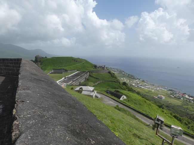 2020年2月19日(水)、今回の旅6日目、セントキッツ島(St. Kitts)の午後。午前中のツアーから午後1時にクルーズターミナルに戻って来て、そのまま町の観光に出ると云うT中夫妻と別れ、私はクルーズ船に戻り、ビュッフェで昼食にする(下の写真1)。食後にソフトクリームを食べ(下の写真2)、屋上デッキのプールを見下ろしながらコーヒーを飲みながら(下の写真3)、午後の行動を考える。<br /><br />午前中のツアーで寄ってくれることを期待していたのだが、海岸沿いの道から見上げるだけだった世界遺産のブリムストーンヒル要塞国立公園(Brimstone Hill Fortress National Park)。やっぱ、どうしてもここは行ってみたい。と云うことで、タクシーをチャーターして行くことにする。2時前に再び船を降りて、入国ゲートを出た辺りで声を掛けてくるドライバーと交渉。50US$で交渉成立！公共交通機関では無理なところのようなので、しょうがない(海岸沿いの道はバスで行けないことはないようだが、そこから要塞まではかなりの距離の山登りが必要なようだ)。<br /><br />2時半頃、海岸沿いの道を山側に折れて、ブリムストーンヒル(硫黄の丘)をどんどん登って行く。坂道の途中の料金所で入場料10US$を払って10分足らずで、海抜約250mの高さにある要塞跡に到着。ここは、17世紀から18世紀にかけてイギリスが建てた、38エーカー(東京ドーム約3.3個)以上もの広さを持つ、西インド諸島最大の要塞の史跡。ほぼ90年間の歳月を費やして、1782年に完成させたもので、建設作業にはアフリカから連れて来られた奴隷の労働力が充てられた。<br /><br />要塞が建てられた頃、イギリスとフランスは島の領有を巡って対立し続けていた。1689年にまずは最初の大砲が設置された。1690年にフランスを駆逐した後、イギリスはここを要塞として造り始めた。1736年までに49門の大砲が設置され、イギリスの西インド諸島攻略の拠点地として「カリブ海のジブラルタル(The Gibraltar of the Caribbean)」と呼ばれていた。<br /><br />1782年にフランス艦隊がこの要塞を攻撃した時、約1,000人のイギリス軍は頑強に抵抗したが、1ケ月後に降伏した。フランス軍は、最後まで戦ったイギリス駐屯軍の英雄的な防御に敬意を表したそうだ。その1年後の1783年にヴェルサイユ条約によりこの島はイギリスに返還され、イギリスはこの要塞の防御力を強化し、以後二度と陥落することはなかった。実際、1806年にフランス軍の攻撃を受けたが、跳ね返した。<br /><br />1834年にハリケーンにより損害を受け、1853年にこの要塞は放棄された。その後はこの要塞は破壊が進むままにされていたが、20世紀中頃になってようやく修復の動きが進み、1975年に一部が公開され、1987年に正式に国立公園となり、1999年にブリムストーンヒル要塞国立公園としてユネスコ世界遺産に登録された。<br /><br />一番高いところにあるのがフォートジョージ砦(Fort George Citadel)で内部は博物館になっている。砦を挟んで西の武器庫(Western Place of Arms)、東の武器庫(Eastern Place of Arms)がある。砦の上からのカリブ海の景色は気持ちがいい(表紙の写真)。西の武器庫からはプリンスオブウェールズ砦(Prince of Wales Bastion)も見下ろせる。<br /><br />車を止めるのはその下のパレードグランド(Parade Ground)だったところで、崖側には歩兵士官兵舎(Infantry Officers&#39; Quarters)跡があり、その奥には砲兵士官兵舎(Artillery Officers&#39; Quarters)跡が続き、モンキーヒル(Monkey Hill)と呼ばれる小高い丘がある。反対側のフォートジョージ砦の下にあるのは食堂(Canteen)と准士官兵舎(Warrant Officers&#39; House)。<br /><br />30分ほどで観光終了。お金は掛かったが、行って良かった。満足！ しかし、1人なので普通の乗用車で良かったのに、10人以上乗れる軽トラ改造バス(?)は無駄だったよなあ・・・(下の写真4)。<br />https://www.facebook.com/chifuyu.kuribayashi/media_set?set=a.4251608124909179&amp;type=1&amp;l=223fe1adec<br /><br />3時半過ぎにクルーズターミナルに戻り、Tシャツやキーホルダーなど土産物をショップで購入(9US$)し、船に戻る。シャワーを浴びてすっきりして着替えた後は、デッキに出て島の景色をゆっくりと眺める。定刻の5時に船は出航。到着した時に既に隣に停泊していたホーランドアメリカライン(Holland America Line)の2016年就航の新しいクルーズ船コーニングスダム(MS Koningsdam)が見送ってくれる。米国のフォートローダーデール(Ft. Lauderdale)を12日に出発して2週間足らずのクルーズ旅行の途中だったようだ。<br />https://www.facebook.com/chifuyu.kuribayashi/media_set?set=a.4238346022902056&amp;type=1&amp;l=223fe1adec<br /><br />この日のここの日没は18:14で、それから30分ほど夕暮れの海を眺めていて、7時にはメインダイニングで夕食。この日は赤ワインで、シーザーサラダ、ステーキ、パフェ(下の写真5)。<br /><br /><br />6日目終了。