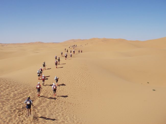 最高気温50度以上最低気温10度以下のサハラ砂漠を、10kgのバックパックを背負いながら、7日間で約230km走破した物語<br /><br /><br />２００７／３／２４　サハラマラソン レース前日<br /><br />サハラ砂漠での本格的な生活の開始。朝食を終えると各自荷物の整理をし、荷物検査へ。<br />７日分の生活物資をここで決断せねばならない。午後は自由時間で、夕方には前日祭が行われた。<br /><br />３／２５　サハラマラソン １ｓｔステージ<br /><br />早朝からベルベル人にテントから追い出され、地べたでの自給自足が始まる。<br />初日の目標は景色を楽しむこと、怪我をしないこと、なにより無難に終わること。<br />明日につなげることが大事。<br />こまめな水分補給を心掛けたが、ＣＰ１までで水が５００ｍｌも減ってない。<br />体調がいいのでさほど気にも留めずＣＰ２も通過して、小高い丘に立つとＢＰ（ゴール）が見えた。<br />一気に行ってしまおうと走り続けたが、なかなか近づかない。これがサハラマジック・・・<br />最後は欧米人と手をつないで笑顔でゴール。<br /><br />３／２６　サハラマラソン ２ｎｄステージ<br /><br />昨日よりもペースを上げた。<br />ただ水分補給は同じペースで行っていたので、それが仇となりフラフラでＣＰ２到着。<br />即刻メディカルに連行され、１時間休憩したあと、「君は脱水症状にかかっている。血圧が低すぎるので点滴をするがいいか？」と聞かれた。<br />ペナルティとのことなので断り続けたが、周囲から説得され、受け入れざるを得なくなった。<br />再スタートするころにはビリになっていた。<br />でも体が復活したので、ドクターにお礼を言って、元気に走り始めた。<br />ＣＰ３過ぎにとてつもない絶壁の山越えがあり、途中動けなくなっていた怪我人を発見し、救助を手伝ったりしながらも、なんとか制限時間内にゴール。<br /><br />３／２７　サハラマラソン ３ｒｄステージ<br /><br />昨日のこともありとても慎重に歩き中心でレースを進める。<br />でも歩き慣れてないせいか、マメの影響もあって足が極限状態まで痛む。<br />特にＣＰ２のあとの砂丘→山越えエリアはひたすら無言で耐えて前進。<br />ゴール後には足のマメは記念すべき１０個を突破。<br /><br />３／２８－２９　サハラマラソン ４ｔｈステージ<br /><br />７０ｋｍ以上のロングステージだが、開始２～３ｋｍで早くも足が痛み出し、走るのをやめて歩き出す。<br />ＣＰ１過ぎで限界に達し、前に進めなくなる。<br />そこへ３時間遅れでスタートしたトップ集団が次から次へとガゼルのように駆け抜ける。<br />彼らの走りに元気をもらい、休みながらＣＰ３まで耐え抜いた。<br />ここで蛍光スティックが渡され、じきに日が暮れた。<br />ここから１０ｋｍ近く続く砂丘はまさに地獄。<br />足は極限状態、砂嵐もやってきて、目印を見失い迷いかける。<br />孤独になると暗黒世界に恐怖さえ覚える。<br />２０時過ぎ、ＣＰ４で寝ることにし、目覚めると朝６時近く。完全に寝すぎた。<br />選手もほとんどおらず、３０ｋｍ先のＢＰで昼食をとることを目標に走り、１３時頃無事生還。<br /><br />３／３０　サハラマラソン ５ｔｈステージ<br /><br />フルマラソンデー。<br />両太ももに巨大な水ぶくれを作りながらもＣＰ３まで頑張って走る。<br />しかしゴール手前約８ｋｍのところで足に激痛が走り、異常なほど巨大なマメが両足にいらっしゃるのに気付く。<br />とりあえずゴールを優先し、そのまま足を引きずり歩いた。<br />抜き去っていく外国人に優しく励まされると、無様な自分が悔しくて、情けなくて何度も涙が出た。<br />ゴールしたときには立っているのも精一杯で、とめどなく泣き続けた。<br /><br />３／３１　サハラマラソン ６ｔｈステージ<br /><br />最終日ともあってスタート前はお祭り騒ぎ。<br />ゴールはワルザザード。<br />長い砂丘地帯では歩きを入れつつも最後は涙を流しながら猛ダッシュ。<br />完走メダルを首からかけてもらったときには、この雄大な大地にすべてを解き放つように涙が溢れ出た。