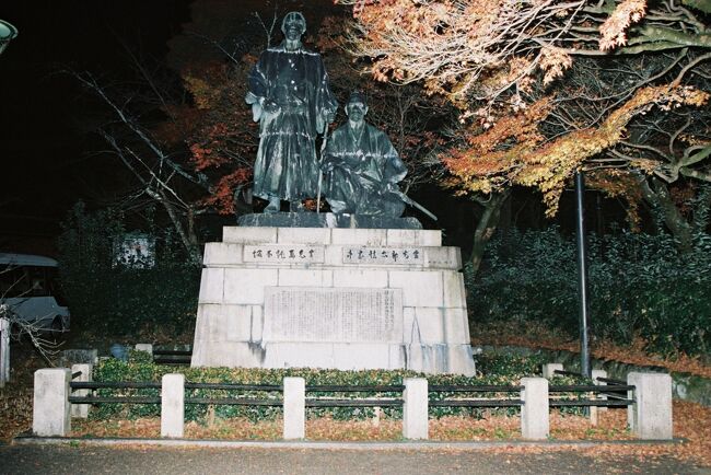 《2020.December》あみんちゅなにげに関西街歩きの旅京都そのⅠ之参~武家の時代・そして近代へ編~<br /><br />高台寺参拝を終えねねの道を南進する。行きにチケットブースが無人だと思ったのは無人の〝観光案内所〟のようだった。しばらく歩くと高台寺と刻まれた石碑があった。駐車場へと向かう坂に繋がっているようで、車ならばこちらから進むことができるようだ。わざわざ石段の続く参道を歩く必要がないことを改めて知った。石碑の隣には維新の道がある。京都霊山護国神社や霊山歴史館の他坂本龍馬の墓もある。今日は時間の都合で行かないが、また改めて来た際には立ち寄りたいと思う。<br /><br />一旦西進すると高台寺表門がある。ライトアップはされているが、境内のように眩しいレベルではなく、重厚感を表現するものとなっていた。ここから北進する道は下河原通となる。カフェ等都情緒溢れる建物を利用したお店は、通常ならば多くの観光客で賑わっていそうだが、このご時世故店そのものが閉まっておりその賑やかさはなかった。途中石塀小道へと入り、The京都という雰囲気を味わう。狭くて入り組んだ路地は圓徳院出口を掠めて家と家の間を通り抜ける小道となり下河原通へと戻って来る。そのまま北進すると八坂神社石鳥居へと道は伸びており、再び東進するとねねの道に合流する。円山公園入口には京都霊山護国神社と頼山陽先生墓碑と刻まれた石碑がある。どうやらこちらからも行くことができるようだが、地図で見る限りわからなかった。京の街を〝碁盤の目〟と評するがあくまで洛中のことであり、その周辺ではどこに繋がっているのかがわからない小道が沢山ある。<br /><br />円山公園に入り先ずは〝例〟の銅像を探す。中岡慎太郎と坂本龍馬の像である。この像は戦時中の金属供出でなくなったものが、戦後に作り直されたものである。武家時代から近代化を推し進める尊王攘夷・大政奉還・王政復古の大号令等を経て明治維新と繋がっているが、この半世紀程の期間に於いて旧幕臣と官軍が争い多くの血が流れている。その犠牲を経て近代国家としての日本に行き着くのは言うまでもないことだが、維新の立役者と言われるこの両名は、グラバーをはじめとする武器商人から新式の銃を購入し、官軍が戦闘を優位に進める方程式を作り上げたことも事実である。戊辰戦争と呼ばれる近代日本に於ける最大の内乱による結果で明治維新となったことは知られているが、内乱と称されるものであれば、もう少し犠牲を減らすことはできなかったのか?と思えて仕方がない。結局思想論で敵対する旧幕臣によって両名は殺害された。そのことを血で血を争う結果だったと考えるのは私だけなのだろうかとふと思った。<br /><br />150年前に想いを馳せつつ円山公園を歩く。そのまままっすぐに進むと神宮道へと入り知恩院の三門が見えてくる。この界隈だが客待ちのタクシーが沢山停まっていた。この時期引っ張りだことなっている筈だが、観光地も含め需要はほとんどないと高台寺公園の喫煙コーナーで話をしたタクシードライバーさんが言っていた。東山の駅まで~と利用することも考えたが、帰り道に立ち寄る場所はほとんどが一方通行の道に面しており勝手が悪い。まぁ明日は我が身と思いながらも帰り道を歩いて行った。<br /><br />古門前通を西進したところに何やら石碑が建てられている場所を見つけ立ち寄ってみる。先求院、知恩院の塔頭のひとつであるが、ここには徳川四天王の一人酒井忠次公の墓所でもあるようだ。しかし実際の墓所は知恩院裏の墓地にあり、この先求院が管理しているとのことだった。この先求院何やら曰く付きの事件があったようで、詳細を調べようとするとその話ばかりが引っ張られてしまう。部外者の立ち入ることではないため、詳細を調べることを諦めて先を急ぐことにする。<br /><br />先求院の先を北進すると大きな学校らしき建物が見えて来る。浄土宗知恩院と関わりのある華頂女子高等学校である。明治44(1911)年に旧華頂宮邸宅跡に華頂女学院を創設したことに歴史が始まっている。以来1世紀を超える歴史を持つ学校ではあるが、少子化に伴う生徒減少が進む昨今に於いて多くの男子・女子高が共学化されているのに対し、華頂女子高は今尚女子校であり続けている。一度高校時代に学祭に呼ばれて行ったことがあるが、うちの高校との違いにビックリしてしまい記憶に残っていないことを思い出した。<br /><br />平日昼間ならば通学の女子高生で溢れている道であるが、この時刻故誰にも会うことはなかった。そのまま白川沿いまで歩いて行った後三条通へと向かって行った。一本橋を越え和菓子の餅寅の角を曲がる。餅寅横にも道標があったが〝明智光秀の塚〟に到着する。時折〝首塚〟と書かれている場合があるが、正しくは〝塚〟若しくは〝胴塚〟である。本能寺の変で信長を倒すも、11日後の天王山の戦いに於いて〝中国大返し〟をした羽柴秀吉軍に大敗した。明智軍本陣裏にあった勝竜寺城へと退却した光秀は、夜の闇に紛れて手勢と共に居城坂本を目指すが、陽が上る頃伏見小栗栖の竹林を歩いていた際に土民の槍によって深手を負った。これまでと悟った光秀はその場で自害して果て、介錯を行った家来がその首を布で包んで隠したと言われている。もっとも首はすぐに近くの農民によって発見され、信長の三男である神戸信孝の下へと届けられ、三井寺滞陣中の秀吉の下に届けられて首実験されたと言われている。その後光秀に味方し磔となった斎藤利三・阿閉貞大の首と共に現在の塚付近の粟田口で晒されたと言われている。その後寺僧や配下の武将によって首は持ち出されそれぞれの場所に埋められて供養されている。光秀の胴塚は刺された〝明智の薮〟付近の観修寺にあるが、首塚の伝承地はいくつかある。この場所は粟田口に程近い場所として、首を埋めた上に供養の五輪塔が建てられたと伝承されている。丁寧に葬られ今尚世話をする方々の手によって綺麗に塚がされていることは心打たれるものがあった。<br /><br />人が近づくと祠の照明が自動でつくようにされた光秀の塚を後にして今来た道を戻る。白川沿いに歩くとまもなく三条通に辿り着き、横断歩道を渡った場所が京都市営地下鉄東西線東山駅1番出入口である。<br /><br />3時間かけて歩いて来た。行きは京阪電車と地下鉄ルートであったが、帰りは先発が六地蔵行きなので地下鉄山科で下車し、JRで帰ることにする。時期遅れの紅葉巡りの旅だったが、意外にもまだ楽しめたことが今回の旅のメリットだと感じた私であった。<br /><br /> 《終わり》