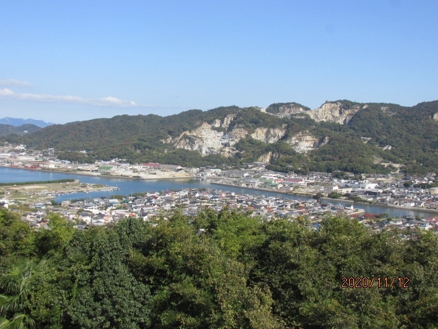 高さ凡そ300m程の屋島山上は平坦な土地になっていて、常の山にあるような峰、ピークと言ったものはない。午前中高松市街を間に置いた五色台にある霊場根香寺からこの島を眺めたが、それは実際来てみても分かることだが、卓状山地、テーブルマウンテンの形状をしていて、殆ど真っ平だった。屋島寺の前の駐車場はその形状を活かせて、広々としたものだ。大型バスでやってくる観光客向けなのか、大きな観光センター、土産物センターの建物も2カ所にあるが、内1カ所しか開いていない。その開いている土産センターもこのコロナ禍では閑古鳥。日本国中、観光業者は至る所カッコーの淋し気な鳴き声しか聞こえてこない。さて先刻この駐車場にやって来た時は、先を急いでいて右下の崖下に見える源平古戦場の跡をゆっくり見ることはできなかった。対岸の八剣山も横目でちらっと見ただけで、車を走らせてきたが、今は屋島寺の巡礼も終わり、少しだけ気持ちの余裕もできた。車をゆっくり走らせ、見晴らしスポットを探しながら、坂を下る。観光道路は部分的に道幅を広げ、何カ所かに古戦場跡の見晴らし台のスペースも作られていて、1-2台車を止めて眼下の景色を眺めているドライバー、家族などもいる。自分も車を止めて崖下の古戦場跡地を見る。見たところ、余り変わり映えのしない埋立地だ。ここが嘗ての戦いの跡とは、道路の案内板がなければ誰も想像はできないだろう。早鞆の瀬にしてもそうだ。古戦場跡の歴史は既に土地の中に埋没し、平家物語や歴史書の中でしか知りようがない。古戦場よりかその先の八剣山、庵治石を切り崩して取り出した、山肌が剥き出た荒々しい傷跡の方がむしろ興味を引いた。ここから切り出された大石は、船で大阪まで運ばれ、あの大阪城の巨大な石組みに使われたのだ。その大阪城築城の400年ほど前、日本の歴史の中で数奇な運命を辿った平氏の栄枯盛衰があった。「平氏であらずば、人にあらず」とまで驕り高ぶった平家一門も最後は壇ノ浦、早鞆の瀬で海の藻屑のように消えて行った。清盛亡き後、源氏の荒武者に京都を追われた平氏一族は神戸福原に仮の都を移したが、そこも又義経を総大将とする追捕の軍に追われ、この地、屋島に逃げてきて、態勢を立て直しつつあったが、それも又義経の奇襲作戦により大敗し、ここから瀬戸内を遁走し、遂には壇ノ浦で清盛の妻時子に抱えられた7歳の安徳天皇は三種の神器と共に早鞆の瀬に身を投じ、平氏一族は胡散霧消した。兵庫一の谷では義経の突然の奇襲に多くの有力武将を失い、ここでも又、徳島経由で後ろの陸地から攻め立てられた平氏軍は一たまりもなく、破れてしまった。先刻屋島寺宝物館に那須与一遺族から寄贈された扇の的の屋島合戦図が展示されていたが、那須与一がこの戦場で勇名を馳せ、同時に平敦盛、佐藤嗣信も戦死した。それから程なく、この時の総大将義経自身が追われる身となり、奥州の地衣川にて無残な最期を遂げることとなった。芭蕉はこの地にはやって来なかったが、何故か屋島寺には芭蕉の奥の細道、平泉で詠んだ句「夏艸やつわものどもの夢の跡」の句碑が立っていた。一の谷には須磨寺があり、ここ屋島には屋島寺がり、壇ノ浦には赤間神宮がある。赤間神宮には耳なし芳一の墓もあり、今でも平家物語は語り継がれている。余り特徴の見られない、埋立地にしか見えない古戦場跡ではあるが、日本の長い歴史の中の一コマを記憶しているのだ。暫し眼下の波打ち際に目を落とし、平家の盛衰を思った。・・そう言えば厳島神社宝物館で国宝の平家納経を見た後、弥山に登り、丁度今の反対側の位置からこの瀬戸内を眺めたこともあったのだ・・。