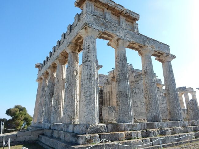 オプショナルツアーでアフェア神殿に行った。パルテノン神殿に似た作りの神殿は、パルテノンのしなやかな姿に比べ、武骨ながっちりとした体形で、柱は太く、一枚岩を切り出した石灰岩で構築されている。<br /><br />島の一番高いと思われる場所に，紀元前5世紀から風雪に耐えて建っている。角に立つ柱に訊いてみた、「2000年以上この場所で立ち続けて、飽きませんか？」と、「ここからはエーゲ海の青とアギアマリーナが見えます。水平線に日輪が上ると、にわかに空気は黄金色に輝き、海の色を変えていきます。海面を吹く風はキラキラと光り、空気が無数の粒々となって舞い上がるのです。それに松の枝を通して吹く風の音が美しいのです。私が誕生したころにはアルカイックな笑顔をたたえた人々がお詣りに来ました、今では平らな顔をした日出ずる国の人々も私に会いに来ます。均整の取れた建物だわね、などと静かにお話をしたりして帰っていきます。時には同じ顔ながら大勢できて、大声で話して雰囲気を壊しながら帰っていく人たちもいます。ここにいると飽きることはありません、でも長い間立ち続けているので、足が棒になってしまいました。」と応えてくれた。<br /><br />32本あったと言われる石柱は、今では24本だけになっている、果たして8本はどこに行ってしまったのか？誰が担いで持ち去ったのか？これを思うと夜も眠れない。