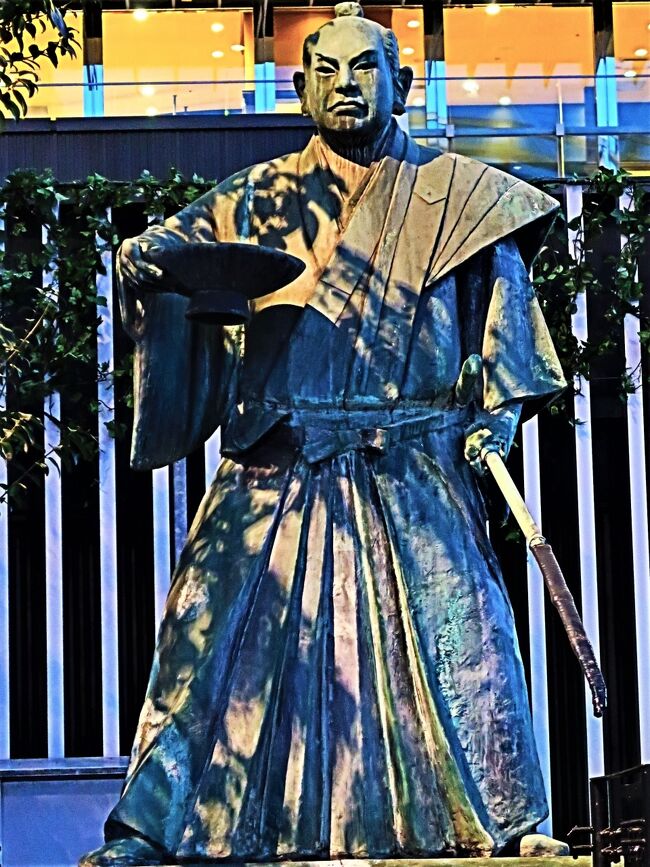 「黒田武士像」 彫刻家米治一製作。<br />1970(昭和45)年設置。 福岡博多ライオンズクラブ寄贈。<br /><br />福岡藩主黒田長政公・家臣で大酒豪の母里もり太兵衛。秀吉伝来の名槍「日本号」を抱え、右手に一尺の大杯を持つ、堂々とした立ち姿です。<br /><br />民謡「黒田節」<br />酒は飲め飲め 飲むならば 日本一の この槍を 飲みとる程に 飲むならば これぞまことの黒田武士<br />峯の嵐か 松風か 訪ぬる人の 箏の音か 駒ひきとめて 立ち寄れば 爪音高き 想夫恋 (歌詩引用:日本コロムビアレコードより)<br /> <br />1942(昭和17)年、コロムビアレコードの人気芸者歌手、赤坂小梅が、レコード吹き込みした頃は、題名が「黒田武士」と表記されていました。 真珠湾攻撃から半年過ぎての発売で、歌詞も戦時下での戦意高揚に一役買いました。 この年、社名を日蓄工業に変更。商標も「コロムビア」から「ニッチク」になります。 敵国用語が使えない時代のエピソードです。<br />戦後1946(昭和21)年、社名を「日本コロムビア」、商標を再び「コロムビア」にします。そして1948年、歌詞を一部変更して「黒田節」の題名で再発売。当時は、占領下の日本でしたので、占領軍(進駐軍)の圧力か、自主規制だったと思われます。<br />https://ameblo.jp/jksta-322/entry-12526979538.html より引用<br /><br />JR博多シティ については・・<br />https://www.jrhakatacity.com/<br /><br />おおやま もつ鍋 については・・<br />https://www.motu-ooyama.com/<br /><br />