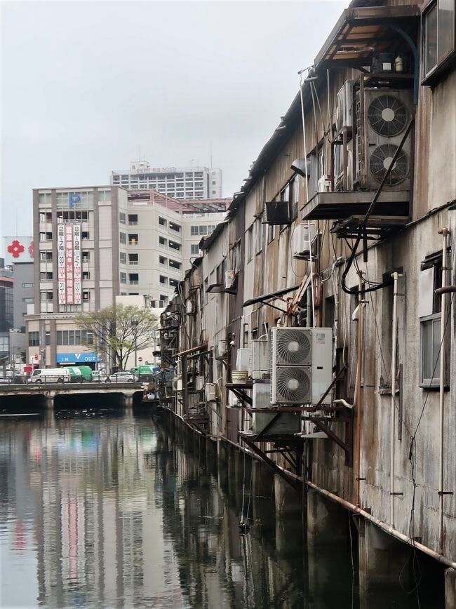 旦過市場 については・・<br />https://www.tangaichiba.jp/<br /><br />旦過市場(たんがいちば)は、福岡県北九州市小倉北区魚町にある市場。北九州の台所とも呼ばれる。<br /><br />神嶽川(かんたけがわ)の東側に位置し、小文字通りをはさんで魚町銀天街に接続している。アーケードになっており、北側入口には長らく日本初の24時間営業スーパーマーケットの丸和があったが、2019年3月1日からは運営主体の変更に伴いゆめマートになった。<br />200店舗以上が軒を連ね、鮮魚・青果・精肉・惣菜などを扱う店が多いが、郷土料理の「じんだ煮」や鯨肉を扱う店もある。北九州市を代表する市場であり、福岡県内においては福岡市の柳橋連合市場と並び称される。<br /><br />主婦をはじめとする一般消費者のみならず、料亭や料理店などの料理人も買い付けに訪れる。グルメ番組や旅番組でしばしば紹介され、観光客も多く訪れる。また、近年は旦過市場の川側とは反対側の裏手に位置する「新旦過横丁」(新旦過飲食街)と呼ばれる場所に、若者をターゲットにしたお洒落な飲食店が営業しており、週末の夜には若者の姿を見ることが出来る。<br /><br />ちなみに旦過とは修行僧の雲水が宿泊する場所で、東曲輪の町屋敷と小笠原家ゆかりの宗玄寺や開善寺などとを結ぶ橋が架けられ、城下町の南玄関の香春口に通じる。<br /><br />大正時代のはじめ、隣接する神嶽川から魚の荷揚げ場として成立し、その後、田川・中津方面からの野菜の集積地となったことで市場としての機能が形成された。昭和30年代に建てられた木造建築物が密集しており、1960年代を時代背景とした映画『初恋』(2006年公開)の撮影ロケーションが行われたこともある。また、中央の通路を挟み川側(丸和側)は建物が神嶽川の上にせり出して建っている。<br /><br />このような環境のため度々災害に見舞われている。 2009年7月の中国・九州北部豪雨、および2010年7月の豪雨では浸水の被害に見舞われた。 2022年4月19日未明には新旦過横丁付近から出火し、鎮火までに約65時間を要し少なくとも42軒に延焼が及ぶ火災が発生した。<br /><br />北九州市では神嶽川の改修にあわせて旦過市場の再整備のための土地区画整理事業を計画し、2021年2月10日に「旦過地区土地区画整理事業」として事業計画が決定した。<br />計画によると、現在の旦過市場の東側(旦過駅前)に4階建てのビルを建設し、ビルの1・2階に約60店舗を収容して神嶽川側へのせり出しを解消する。再整備にあたっては区域内の店舗を順次仮区画へ移転しながら営業を継続するローリング方式を採用し、2027年度の完成を予定している。なお、2022年の火災で大きな被害を受けた新旦過横丁は土地区画整理事業のエリアに入っていない。<br />(フリー百科事典『ウィキペディア(Wikipedia)』より引用)<br />