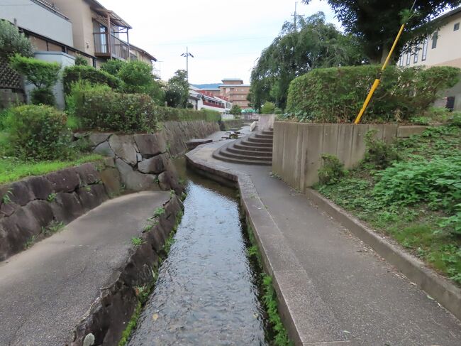 2021年7月14日(土)6時前、稱名寺からさらに北に進むと古世親水公園に突き当たる。亀山城の外堀跡で、当時は家老屋敷や石高の高い上級武家屋敷が配置された三之丸と、中級や下級武家屋敷に商人町が配置された外町とをこの堀で分けていた。江戸後期の1793年の古地図によるとこの辺りには馬見所と騎射組が置かれた桜の馬場と記されており、馬廻り関係の藩士の居住区だった。<br /><br />西側の湧き水が噴き出す辺りはハナショウブが繁っており、ひと月ほど前には咲き乱れていたものと思われる。湧き水の水源は市街地の東側を横切って大堰川に注ぐ年谷川の伏流水。ハナショウブ畑の隣に建つ建物は野菜の洗い場。この湧き水は古くから飲料水や炊事、洗濯、洗い物といった生活用水にも利用されていた。<br /><br />洗い場の下流が1988年に整備された古世親水公園。上流からの豊かな湧き水が流れる深さ10㎝程度のきれいな小川を挟んで通路が造られ、外堀の石垣をイメージした宝伝石を使った護岸が北側に並ぶ市民の憩いの場となっている。下流部の川幅が広くなった部分には飛び石も置かれ、水遊びが出来るようになっており、夏には子どもの絶好の遊び場となっている。<br /><br />洗い場の西から少し北側、亀岡高校のグランドの南側には王地山稲荷大明神がある。江戸中期の1748年に丹波篠山の領主であった松平信岑(のぶみね)が、亀山藩へ転封される際に、篠山にあった稲荷大明神を亀山城にも勧請したことに始まる。五穀豊穣、商売繁盛、勝負に勝つなどのご利益がある。<br /><br />元々は、関ケ原の戦い直後の1601年に、常陸の土浦城主となった藤井松平信吉が、霊感を受けて妙長山本教寺を建立し、その鎮守として右手に剣を持ち、左手に玉を捧げ、白狐に乗った荼枳尼天王、すなわち神仏習合の姿、稲荷大明神として祀ったもの。信吉が1619年に篠山藩主として転封する際に、領国篠山の王地山に本教寺を移し、同時に鎮守であった稲荷大明神も遷座し、王地山稲荷大明神と呼ばれるようになった。<br /><br />このお稲荷さんは負け嫌い稲荷とも呼ばれている。江戸時代の話で、両国の回公院で毎年春と夏に将軍上覧の各藩対抗の相撲大会が開催されていたが、亀山藩の力士はいつも負けてばかりいた。がある時、連戦連勝で勝ち進んだ力士が現れた。藩主は慰労して褒美をつかわそうとしたが、その力士はこつ然と姿を消していた。その後この力士はこの王地山稲荷の化身であると分かり、絵馬や幟を奉納し、勝利の守護神として厚く信仰されるようになったそうだ(下の写真1)。同じ話が篠山の稲荷大明神にも伝わっているそうだ。<br />https://www.facebook.com/media/set/?set=a.7636235426446415&amp;type=1&amp;l=223fe1adec<br /><br />お稲荷さんから西に進むと、亀岡高校グランドのフェンスに説明板がある。前述の桜の馬場の記載があった古地図にはこの辺りは三の丸の南東部で城内側の御土居付近に土手丁として載っている。三の丸の武家地に当たり、藩士の武家屋敷が連なっていたようだ。<br /><br />以上で初めての亀岡散策を終了して、線路を越えて北側のサンガスタジアム by KYOCERAへ移動、サッカーのなでしこジャパンの東京オリンピック前最後の練習試合となるMS＆ADカップ2021のオーストラリア代表戦を観戦した。<br />https://www.facebook.com/media/set/?set=a.6010454472357860&amp;type=1&amp;l=223fe1adec<br /><br />以下、簡単にサンガスタジアム by KYOCERAについて触れる(下の写真1)。正式には京都府立京都スタジアムと云う球技専用競技場で京セラ(株)が開場時から10年間のネーミングライツを得ている。2020年1月に竣工式が行われ、2月9日にこけら落としのサッカープレシーズンマッチ、京都サンガ対sセレッソ大阪戦が開催された。<br /><br />京都では1995年から新スタジアムの建設が検討されたが具体化まで進まず、2006年に計画は白紙となった。2010年に改めて京都府が球技場新設の検討を開始、敷地の無償提供を条件に候補地を募ったところ、亀岡市、城陽市(木津川右岸)、舞鶴市(青葉山ろく公園)、京丹波町(園部)、京都市(横大路)が申し出たが、検討の結果2012年12月に亀岡市に決定。<br /><br />2013年から具体的な計画の立案がスタートし、2016年4月から着工予定となったが、天然記念物アユモドキの生息への影響が問題化し、計画は再検討となり、当初の建設予定地より300m南に変更され、2018年1月にようやく起工となった。位置がずれたことで亀岡駅北口にほぼ接するようになり、非常に便利になった。京都駅から快速に乗れば30分以内にスタンドまで入れる。<br /><br />そのスタンドは地上4階建てで高さ27.6m。収容人員は21.623人で、全ての観客席が屋根に覆われている。よほどの嵐じゃない限り雨に濡れることなく快適に観戦が出来る。全国津々浦々のスタジアムに行ったが、交通の至便性にしても、観戦のし易さにしても、トップクラスと云える。<br /><br />なお、スタジアムにはフィールドだけでなく、スポーツクライミング施設やVR/フィットネスゾーン、eスポーツゾーン、コワーキングゾーン、3x3バスケットボールコート、貸会議室、フードコートも備えられており、サッカーやラグビー、アメリカンフットボールなどのスポーツやライブイベント以外にも利用できるほか、保育園も開園している。<br /><br /><br />以上で、初めての亀岡散策の記終了