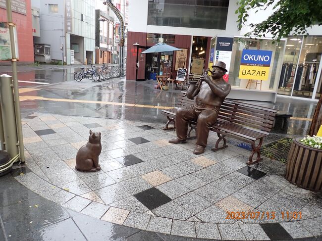 タイトル写真は、「サキソフォン吹きと猫」の像です。<br />今回は希望する富良野の宿が予約出来なかったので、旭川で8泊して美瑛や富良野を定期観光バスなどを利用して散策します。<br />旭川電気軌道のバスで旭川駅に向かいます。北海道の中では札幌市に次いで2番目に大きな都市なので、駅前の交通量も多かったです。<br />チェックイン前に、旭川観光物産情報センター、イオンモール旭川駅前に立ち寄った後、ホテルにチェックインします。ＪＲ旭川駅からは少し歩きます。<br />このホテルがなかなかユニークでした。夕方のハッピーアワーは早い者勝ちですが、カレーライス、ドリンク（アルコールも数種類有り）、おつまみをゲットできます。ランドリーは乾燥機も含めて無料でした。<br />市内のメイン通りの一つである平和通買物公園に出かけます。<br />「サキソフォン吹きと猫」のモニュメントは、雨で猫もオジサンもしっかり濡れていました。<br />残念だったのは、コロナの影響なのかもしれませんが、平和通買物公園にあるmarukatsuさんは閉鎖されてました。大きいショッピングモールが閉店したのは、ＪＲ旭川駅直結のイオンモール旭川駅前の影響が出ているのかもしれません。「フィール旭川」さんは、元気に営業してました。<br />ＪＲ旭川駅に戻って、アイヌ文化情報コーナー「ル シロシ」とちょっと変わったスタイルで有名な石川啄木像・歌碑を見学して、その１終了です。、<br />