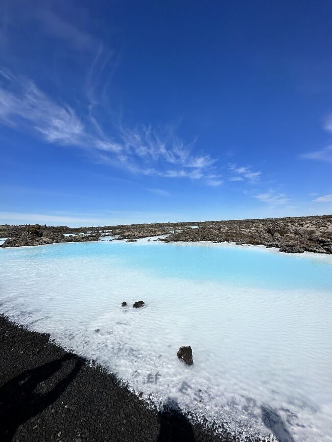 　もともと２０２０年に予定していたアイスランド旅行はパンデミックにより中止になり、今回やっと実現となりました！<br />大都会よりも大自然派の私たち夫婦は日本と比べてスケールが桁違いのアイスランドの自然を満喫するべく、計画を立てました。<br />　羽田空港からフィンランド・ヘルシンキ経由でアイスランド・ケプラヴィーク空港へ。ホテルに手配をお願いしていたタクシーにてホテルに直行。１泊目はNorthern Light Inn。まだ朝だったにも関わらずお部屋に通していただきました。<br />　午前中はホテルの周りを少し散策して、見渡す限りの苔に覆われた溶岩台地に感動しました。なんだか広大すぎて遠近感がなくなる感覚です。アイスランドらしくずっと風が吹いていて、タクシーのドライバーさんにも風が強いですねって言ったら「そうさ、だってここはアイスランドさ」という返事。<br />　ヘルシンキでの乗り換え時に買って余っていたサンドイッチをランチに頬張った後、ホテルから歩いて１５分ほどにあるブルーラグーンへ。ここのチケットは日本で予約を取ってありましたので、受付もスムーズ。タオルなどを借り水着に着替えて念願のプールに！水温は熱くもぬるくもなくちょうどいい湯加減。塩分があるそうなので、指がふやけてくることもありません。ドリンクバーで一杯もらったりして１時間くらいは入っていました。<br />　夕方はゆっくりしてからホテルのレストランにて夕食。窓から見えるゴツゴツした台地、木の生えていない山や地熱発電所の湯けむりを眺めながらなかなか日の沈まない夜が始まりました。<br /><br />＊＊＊＊＊＊＊<br />旅程（★いまここという印）<br />★7/16　JL047　JAL（羽田 22:50 → ヘルシンキ 06:35 + 1)13時間45分<br />★7/17　AY991  FINNAIR (ヘルシンキ 07:45 → レイキャビク 08:25)3時間50分<br />　　　ブルーラグーン<br />　7/18　レイキャビク　ヘリでの火山見学<br />　7/19　レイキャビク　釣り<br />　7/20　2泊3日のゴールデン・サークル、サウスコーストのツアーに参加<br />　7/21　同上<br />　7/22　同上<br />　7/23　レイキャビクでゆっくり<br />　7/24　スナイフェルスネス半島日帰り<br />　7/25　レンタカーでゴールデンサークルの一部とレイキャネス半島ドライブ<br />　7/26　FI546 Icelandair (レイキャビク 10:30 → パリ 15:55)3時間25分<br />　　    JL046 JAL (パリ 19:00 → 15:45+1)13時間45分<br />　7/26　15:45 羽田着