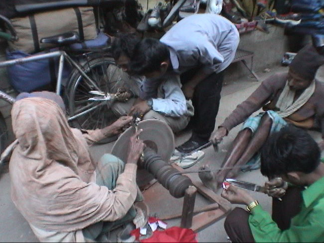 研ぎやさん（カトマンズ・インドラチョーク）<br /><br />●弟子（たぶん）がチェーンをひっぱて砥石を回し、親方（たぶん）が研ぐ。威厳のある顔つきなので、いかにも切れそう。