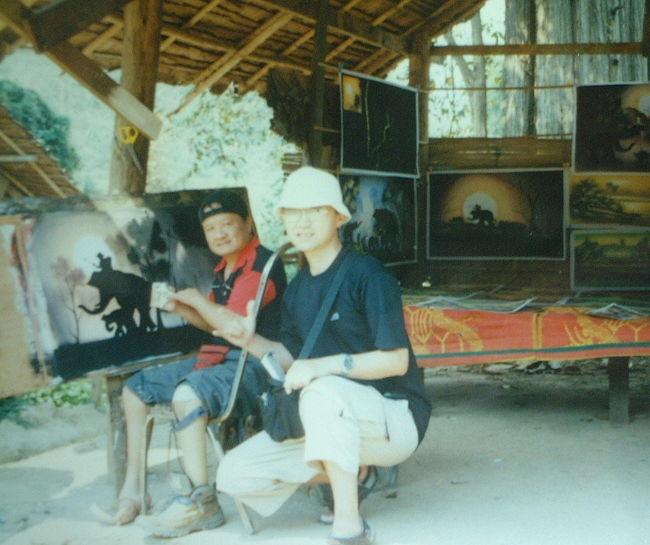 絵描きのムアイさんは、ロングネックガールズの村で、村の入り口で絵を描いている。気さくなとてもイイ人である。手も足も不自由なのに・とても明るく笑顔がイイ。１日かけて描く絵の値段は２００バーツ・６００円。バックパッカーの自分は絵を持ち運ぶ手段がなく、絵を買えなかった・・。