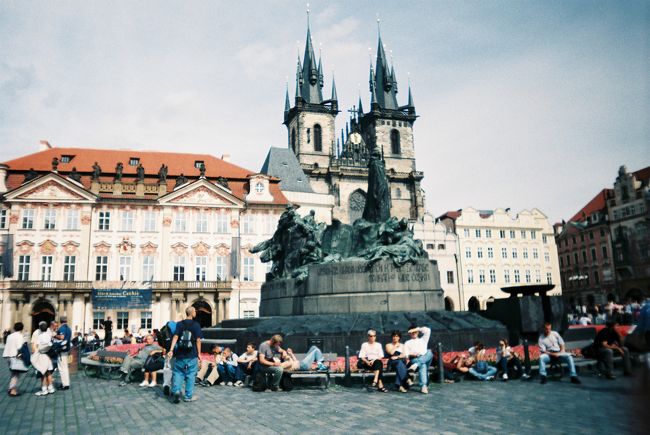 カレル橋を渡り、旧市街広場に着きました。中央の銅像は、火あぶりになった宗教改革者ヤン・フスの銅像です。<br />銅像の奥、左側の建物はキンスキー宮殿。その右側（フスの後ろ）の建物は、ディーン教会です。