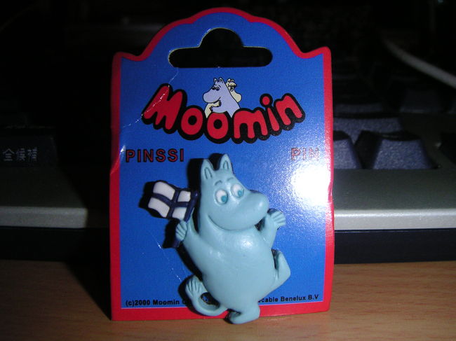 そのムーミンショップでいろいろ土産を仕入れましたが、中でもフィンランドとムーミンがコラボされている（？）一品をご紹介。<br />フィンランドの国旗を掲げてるムーミンピンバッジ。ゴム系の柔らか素材でできています。お値段３．９ユーロ。