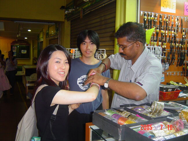 リトル・インディア・アーケードのアクセサリー屋でブレスレットを物色。<br />愛想のいいおじさんが試着をさせてくれてます。<br />ピンク色の物をつけているけど、実際買ったのは緑系とゴールドの豪華な物。