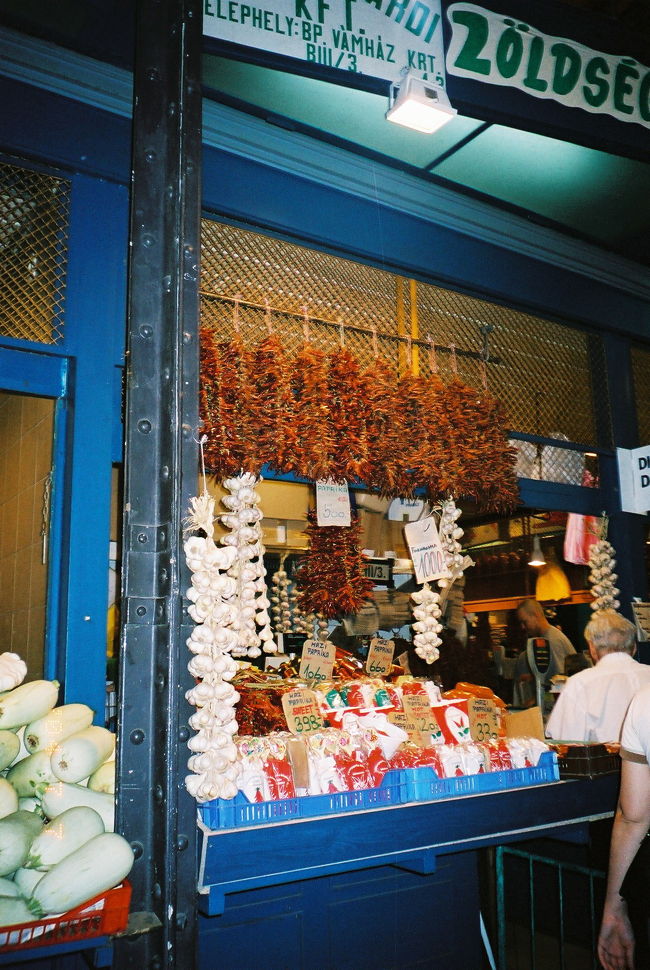 ★中央市場 (V&amp;aacute;s&amp;aacute;rcsamok)<br /><br />中央市場は、内部については、ガイドブックや本で写真をよく見かけるので、行く前からよく知っているような気になっていました。外観については、モザイク屋根のれんが造りの建物で、一見の価値あり、という程度の情報をどこかで拾いました。近づいてみたら、ああ、これか！とひと目でわかりました。市場の建物とは思えないくらい、かっこいい建物です。れんが造りのせいか、なんだかアカデミックなかんじがしました。あるいは、アカデミック、というのは、隣に大学があるせいで、勝手にそう思ったのかもしれません。でも、この中央市場の建物も大学の校舎の一部といわれても遜色ない気がしました。<br /><br />中は、思ったより混んでいませんでした。思ったより広々として、明るいです。どうやら私は、狭いところに物も人もぎゅうぎゅうにひしめいているアラブやアジアの市場のようなところを想像していたようです。よく見ると、ここも一店舗あたりのスペースがそんなに広いわけではなく、品物だって、ぎっしりところ狭しと並べられていました。たぶん、中央市場の建物自体の天井がとても高いせいもあったかもしれません。市場は、地上は2階までしかないが、建物の高さは5階分くらいありそうです。2階から見下ろすアングルがいいと聞いていたので、真っ先に上って見下ろしてみたら、屋台のプレハブ屋根ばかり並んでいて、いまいちでした。これのどこがいいんだ、とがっかりしました。<br /><br />2階は、軽食スタンドとおみやげ屋でぎっしりでした。ちょうど昼食時なので、噂のランゴーシュ (lang&amp;oacute;s) を昼食代わりのしようと、スタンドを探しました。ランゴーシュとは、生地を丸く薄く延ばして油で揚げたパンみたいなもので、ハンガリーでポピュラーな食べ物らしいです。中央市場でも売っているとのことなので、ぜひ試してみようと思っていました。食べている人を見つけました！　いかにもおいしそうです。値段は120HUF（約70円）、安いです。ちょうど揚げたてをいただきました。サクッとした食感で、ほんのり塩味がきいていて、とても美味しいです。これは日本人の口に合うと思いました。<br /><br />（写真は、1階の店の一つです。店先に干しパプリカや玉ねぎが千羽鶴のように吊り下げられている様がおもしろくて、きりがないくらい撮影しました。）