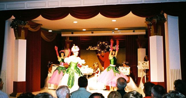 ★ワルツとオペレッタのコンサート (Walzer und Operettenkonzerte)（ヴェレシュマルティ広場のジェルボー・ハウスの中庭の会場（Gerbeaud theatrium）にて）<br /><br />夕食は味付けが濃かったので、のどが渇きました。ワインも飲んだので、疲れがでて少し眠くなってきてしまいました。今晩のコンサートの前に眠気を覚まさねば！───コンサート会場のあるヴェレシュマルティ広場に早めに着いたので、広場に面したカフェでもう一杯、コーヒーをとることにしました。カフェは、ジェルボー・ハウスにしました。コンサートはこの建物の中庭の会場で行われます。覚えがある名前なので「地球の歩き方」をひっくり返してみたら、載っていました。このカフェは1858年創業で、皇后エリザベートも常連だったそうです。ロココ様式の天井やシャンデリラやテーブルは一見の価値ありだそうです。なるほど、私などにはもったいないくらい、由緒ある上等なカフェらしいです。多少、値段が割高でも行く甲斐はありそうですた。<br /><br />なので、どうせなら屋内のテーブルに座りたかったのですが……。しかし、外のテーブルに客がいても、中には誰もいないように見えます。あきらめて広場に並ぶ外のテーブルに座り、ウエイターを待ちました。中はチラッと覗くにとどめました。でも、よく見えませんでした。<br /><br />コンサートは自由席で、ブダペスト観光1日目の晩のバレエ・ガラの会場同様、ここもまた、前の席との段差がありませんでした。仮設会場だから仕方がないのでしょう、と、このときは思いました。でも、考えてみたら、昔の劇場は段差がありませんでした。後で、チェコ旅行中にお城を見学し、付設の劇場などを見学したために気が付きました。とすると、このコンサート会場も、別に夏のハイシーズンの観光客目当ての催し物のための仮設会場、というわけでもなかったかもしれません。<br /><br />カフェが会場から近いのをいいことに開演時間ぎりぎりまでのんびりしてしまったせいで、前のほうの席はすでに埋まっていました。自由席なのですから、早めに来ていてよかったのです。でも、舞台は充分高さがあったので、それほど見づらくはありませんでした。バレエと違って、コンサートで歌手の足元が見えないのはそれほど気にならないことですし。<br /><br />楽団は女性だけの室内楽団で、唯一、指揮者だけが男性でした。女性は全員、ピンクのドレスを着て、髪に花を飾っています。それだけでパッと舞台が華やかになります。指揮者もピンクのタキシードです。<br /><br />歌手やダンサーは交代で出てきましたが、女性は毎度、ドレスを替えてきました。同じ衣装で出てきたことは一度もありませんでした。イブニングドレスや、まるでウェディングドレスのようなうっとりする衣装もあれば、バラそのものの形をした帽子をかぶってきたり、水色と白の縞模様にハイビスカスのハワイ風の、舞台じゃなきゃ着れないね、ってかんじのカラフルな衣装だったり。ハンガリーの民族衣装っぽい衣装のときもあり。かといって、昨日の民族舞踊のコンサートの素朴な村娘の晴れ着というのとは全く印象が違って、舞踏会のドレスを民族衣装風にアレンジしたというかんじでした。そしてどの歌手も美人で、あるいは可愛らしくて、衣装がとても似合っていて、次々変わるファッションを見ているだけでもわくわくしました。男性の衣装は女性のほどヴァラエティがなく、黒の燕尾服と白い蝶ネクタイの正装で決めてくることも多かったですが、女性にあわせてカラフルな服のときもありました。私はオペレッタは見たことがありませんが、たぶん、これがオペレッタらしいんだろうなぁというかんじの華やかな衣装に、陽気で楽しい歌に音楽。観客を楽しませようとするちょっとした演出。とにかく、目にはきらびやかで、耳には心地よく楽しく、私のミーハー心をとても満足させてくれたコンサートでした。<br /><br />（写真は、ちょっとわかりにくいと思いますが、歌手がバラそのものの形をした帽子をかぶって出演してきたシーンです。歌専門の人とダンス専門の人とに分かれいて、その背後で両手を挙げて回っている２人はダンス専門でした。）