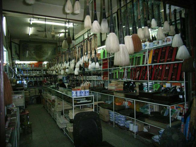 　　買い物は難しい。日本にいると物の価格は絶対的なものだと思ってしまう。原価・手間賃・運送費、それに儲けを足して、売り手が値段を決める。<br />　こちらでは違う。買い手が品物の価値を判断して買いたい価格を決める。売り手は買い手を見て、いくらで買ってくれそうか考え交渉する。交渉が成立したら、それがそのものの値段だ。金持ちの外国人には高く売りつけられて当然だし、自分にとって価値があると思ったら買えばいいのだ。<br />　写真は書院門古文化街の筆や硯を扱う店。天井から筆が所狭しと吊り下げられている。