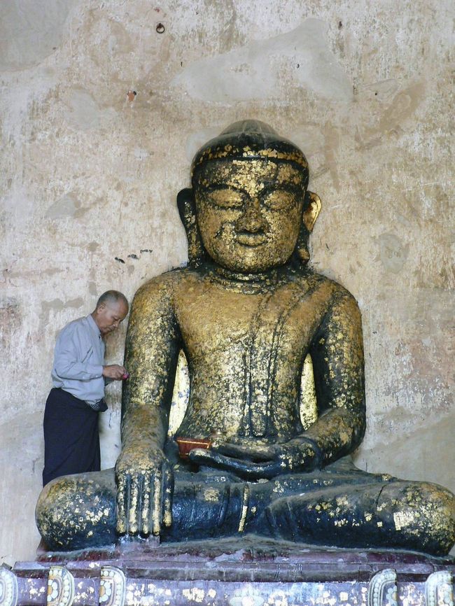 スラマニ寺院で金が剥がれている仏像に金箔をはる人。