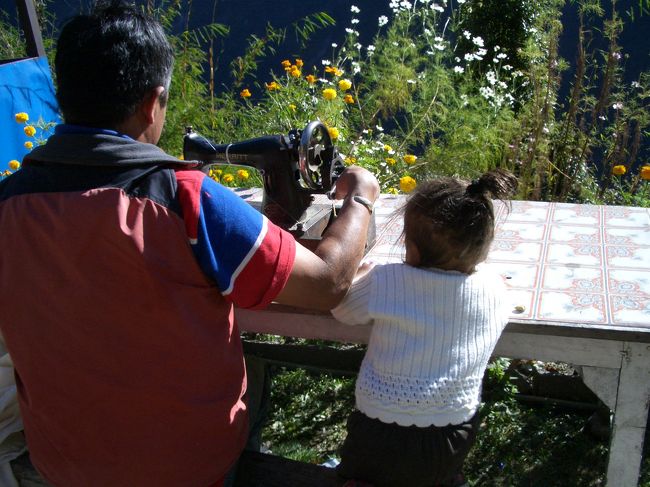 野外の陽だまりは作業場。<br />きれいな花の咲く中で。<br />手動のミシンは動きます。