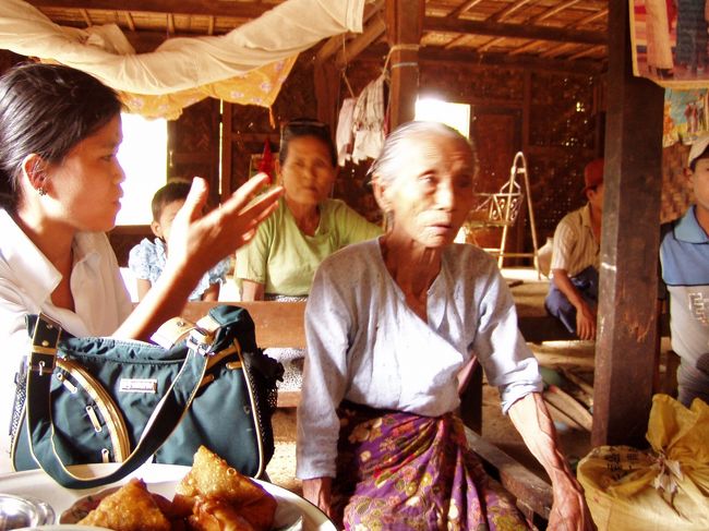 　車で30分は走っただろうか。エイヤワディ河沿いのレッパンチバウ村に着いた。ウィンウィンのおばあちゃんがいる村である。車一台がせいぜいの狭い路地を通ると、周囲の住民の注目を浴びた。村自体は家屋もきれいだし、道路も掃除されていて、ニャウンウーの周辺にある標準的なレベルの村と同じくらいに見えた。<br />　おばあちゃんの家は土間と床に分かれていて、そこそこの広さだった。電気はなかったようだ。<br />　手前の右がそのおばあちゃん。齢80を越えている。ミャンマーでは珍しく長生きと言えるだろう。後ろは妹。このおばあちゃん、実は子供を12人も産んでいる。そして、その娘の一人でウィンウィンの母親は8人も子供を産んでいる。超多産系の母娘だ。少子化対策大臣に引き合わせてやりたい。それだけ丈夫だから長生きもできるんだろう。<br />　ここでひとまず一服し、近くの小学校に生徒が揃うのを待つという。僕は金しか出していないので、その辺の手配はウィンウィンにまかせっきり。結局、現地まで来ても金しか出さない国際貢献なのだ。これではまたまた国民の批判を浴びそうだ．．．ってこれはおれの金なんだよ。<br />　お茶とお結び型の春巻きを出された。春巻きは、まあ普通の春巻きの味がした。ドライバーも中に入ってきて、床に腰掛けている。家族が時折「あんたもどう？」とすすめるのだが、「いや、いいです」とかしこまっている。<br />　ここで15分ほどいて、再び車に乗り込み、近くの小学校へ行った。<br />　<br />