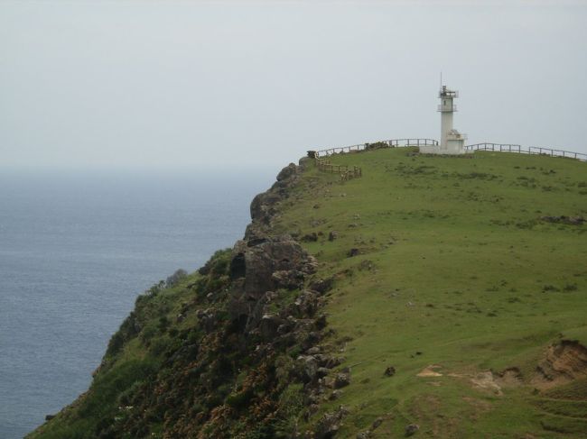 東崎（あがりざき）灯台。<br />石垣島からの飛行機で左窓際の席に座ると、<br />最初に迎えてくれるのがこの灯台だ。<br />青い空、青い海、断崖絶壁の上に白い灯台。<br />なんて素敵な風景だろう。<br />ただし、これで馬糞臭くなければね…