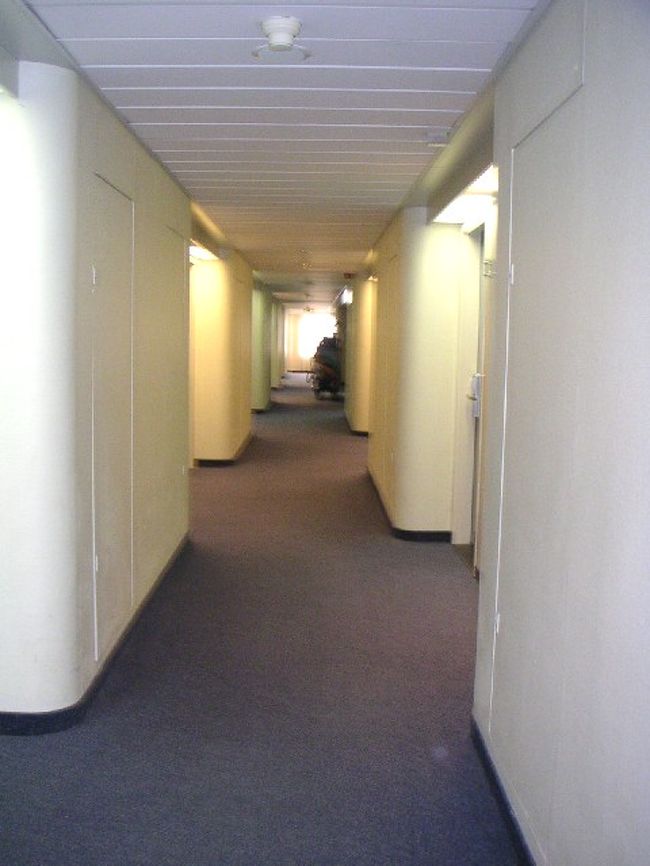 エレベーターホールから廊下を見る。<br />部屋も廊下も全体に明度は低めです。ホンの少し暗い感じがします。