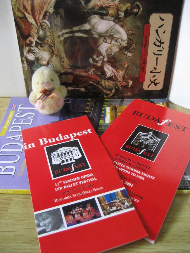 ★ブダペスト夏の音楽祭ブダフェスタ (BUDAfesta) のハンガリー国立オペラ座ソロイストたちによるバレエ・ガラ公演（ホテル・ヒルトンの中庭のヒルトン・ドミニカン・コートにて）<br /><br />会場は野外なので、雨天の場合、開演を1時間ずらしても上演できそうになければ、翌日の7月6日に延期される、と、ちらしにもチケットの裏にも書いてありました。確かヨーロッパの夏は雨が少なかったと思うので、私はこれは、本当に本当に万々が一のことで、形式上、雨天時の予備日を設定しなくてはならないことにでもなっているのかと思っていました。ところが、もうすぐ時間だって頃になって、雲行きが怪しくなってきて、雨が降ってきたではありませんか。<br /><br />そんなぁ、明日に延期されたらどうしよう。明日は民族舞踊のコンサートの予定をすでに入れているのに。<br /><br />フェスティバルの中でバレエ・ガラ公演予定は、5日と7日だけです。雨天の場合、5日の公演が6日に延期になるのではなく、チケットを7日のものと交換してくれないかしら。どうせ自由席だし。7日の夜なら、まだ予定を入れていないため、あいているのです。でも一番いいのは、雨が止んで、予定どおり今晩、上演されることです。やきもきして待ちました。私もそうでしたが、自由席であるため、すでに席を陣取った人々は、カサをさしたまま誰も席を立ちません。小雨なので、カサもささずに構わず座っている人もいます。そう、ヨーロッパの天気は変わりやすいのです。少しの雨ではカサをさす人が少ないくらい。日本と違って雨が降り出したら、もう当分止まない、ということはありません。しばらくすると係りの人が現れて、この分ならやみそうなので、少し待ちましょう！と告げました。たちまち観客席から拍手があがりました。だってね、せっかく来たのに、出直すのは誰だってイヤですよね。<br /><br />一度、雨が止みました。ホテルの人がモップで舞台の上の水を拭きとりました。いよいよ開演か！と思ったら、また少しだけ雨が降り出してきました。この状態で押し切って開演されるのかも、と期待していたら、我々はいいけど、ダンサーにとってはリスキーだね、と誰かが話しているのが聞こえてきました。確かにそうですけど！　やっぱり延期してほしくないです。上演してくれないか、と強く願いました。上空を見上げると、風も強いせいで、雨雲は目に見える速さで流れています。これなら雨が止むかもしれません！───期待しては消沈し、また期待して、の繰り返しでした。<br /><br />結局、開演時間は30分遅れましたが、雨の気配はすっかりうせて、無事、上演されることになりました。感謝！<br /><br />（写真は、ブダフェスタのちらしとプログラムです。それに、ブダペストで買った日本語の「ハンガリー小史」も添えました。この写真は、2004年当時の旅先ではなく、2006年3月に初めてデジカメを買った後に撮ったものです。「ハンガリー小史」は、写真や歴史画、地図などが多くて、山川出版社のなつかしの「世界史総合図録」を思い出させたせいもあって、買ってしまいました@）