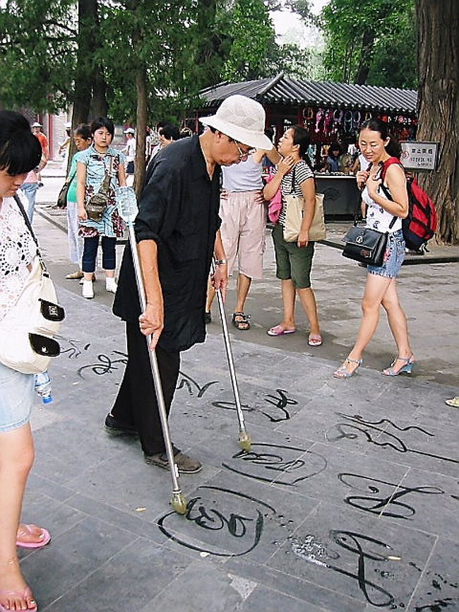地面の石に字の練習をしている地元の人。<br />水が出るように工夫された筆を使っている。