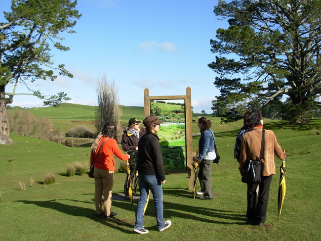 ホビット村ツアーの様子。ガイドさんがたくさんの説明を英語でしてくれた。この時期は快晴と思っても突然の大雨が降るので傘を貸してくれた。また風も強く防寒装備は欠かせない。一見美しい緑も実は羊の糞だらけで、靴の糞落とし器具も置いてあった。