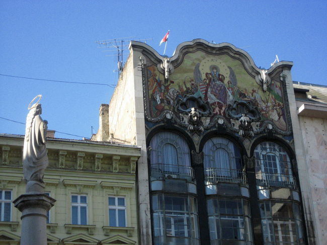 セルヴィータ（Szervita）広場のアールヌーヴォーチックな建物とマリア柱像<br /><br />デアーク広場からヴェルシュマルティ広場に行きたいのに、方向音痴の私はかなり遠回りしてしまいました。<br />前にも行ったことがあるから、と、通りの名前を確認せずに、こっちの方角だったに違いない、と自分の勘に頼って歩いたからです。<br />方向音痴だって自覚しているのに、つい勘に頼ると、必ず方向を間違えます。<br />だから方向音痴だっていうのに、懲りずに何度もやってしまう私。<br />でも、こんな素敵な広場を見つけたので良しとしましょう。転んでもただでは起きないってところかな。<br /><br />ただ、天気はとても良いのですが、写真を撮るにはいまひとつ都合悪い点があることに気付きました。<br />逆光だと対象がかなり暗くなってしまうこと。<br />光と影のコントラストが強すぎて、影の部分が真っ暗になってしまうこと。<br />といっても、曇り空の下だと建物や風景の魅力が半減することがあるし、曇り空のぼんやりした白っぽい空よりは、青空を背景とした写真を撮りたいので、曇りよりは晴れの方がやっぱりいいんですけれどね。<br /><br />この建物は、残念ながら逆光でした。露出をかなりプラスに調整しました。<br /><br />アールヌーヴォーチックと思った建物は、「トルコ銀行」だとあとでわかりました。<br />1906年のアールヌーヴォーの建物です。<br />私の目を引き付けた切妻のモザイク画は、ロート・ミクシャによる「ハンガリーの栄光」と題するモザイク画です。<br />聖母マリアとそれを囲む天使、ハンガリーの英雄が金色のモザイクを背景に描かれているそうですが……ちょっとこの写真では確認しづらいですね。<br />その場にいるときにも、逆光で見づらく、高いところにあったので、どんな絵かよく確認できませんでした。<br />（参考：「世界の建築・街並みガイド５」川向正人・監修、エクスナレッジ発行）