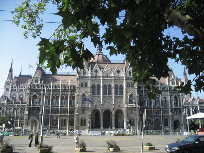 ハンガリー国会議事堂<br /><br />議事堂内部を案内してくれたガイド（もちろん、現地催行バスツアーガイドとは別の人）が、「こんな小さな国にこんな大きな国会議事堂」と謙遜していましたが、ハンガリー国土が今の３倍はあり、ブダペストが最も繁栄を謳歌し、急速に発展した時代を体現している１つがこの国会議事堂です。<br />前から見ても後ろから見ても横から見ても優美な姿@<br /><br />1885〜1904年建築<br />「ネオ・ゴシックを基調にルネサンスを加味した折衷様式で、尖塔付きのドーム、連続アーチと林立するピナクルが華麗。内部では明るく採光された軽やかなクーポラ、金で彩られたレースのような繊細なリブが見所」<br />（「世界の建築・街並みガイド５」エクスナレッジ発行より）<br /><br />この写真は、国会議事堂見学が終わった後に、道路挟んで民族博物館のある歩道から撮ったものです。<br />このとき、議事堂前では、ポップでロックな音楽が大音響で流れていました。<br />歌詞はわからないのでどういう内容の歌かわからないのですが、デモの話を聞いていなかったら、私はきっと呑気に、今、国会議事堂前でお祭りをやっているんだ〜！と思ったに違いありません。
