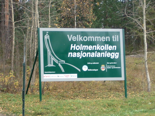 オスロにて是非訪れたいと思っていた場所は3箇所ありました。そのうち建築博物館は訪れる事はできませんでしたが、国立美術館とここホルメンコッレンジャンプ場には訪れる事ができました。<br />ジャンプ場へはオスロ中央駅より地下鉄1番に乗って向かいました。朝早いというのに観光客で電車はいっぱいでした。<br />駅を降りてかなり急坂を5分くらい登っていくとこの看板が見えてきます。ジャンプ台まではあと5分くらい急坂を上がっていきます。