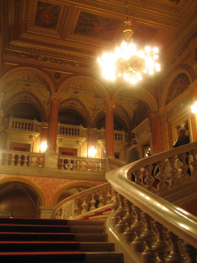 オペラ座入口ホールの階段<br /><br />チェスの駒のような支えのついた階段。<br />黄金づくしの壁や天井。赤い絨毯。<br />ううーん、素敵です@<br />この階段にエルケルの銅像があったはずなのですが、そうと気付かず、無視してしまいました。<br /><br />この階段を上ると休憩所や２階以上の席に続きます。<br />私の座席は１階の正面の方の15列目。座席に行くにはこの階段を上らず、そのまま左に進みます。<br />写真を撮るために少し上ったのです。<br />クロークに荷物を預けましたが、有料でした。120フォーリント。<br />（2006年10月現在、1フォーリント＝約0.6円）<br /><br />「ネオルネッサンス様式の壮麗な建物。音楽大国ハンガリーが誇るヨーロッパ有数のオペラ劇場だ。1873年に建築が始まり1884年に完成した。建築家はイブル・ミクローシュ。その他、画家のロッツ・カーロイ、タン・モール、セーケイ・ベルタラン、彫刻家のシュトローブル・アラヨシュなどが携わった。」<br />「100年以上の歴史を持つこの劇場は第２次世界大戦の戦禍を免れ、1945年３月には公演を再開したという幸運な劇場だ。（中略）一歩足を踏み入れると、そこには外の喧噪とはかけ離れた華麗で重厚な別世界が広がっている。」<br />（「地球の歩き方　ハンガリー　2004〜2005年版」（ダイヤモンド社）より）