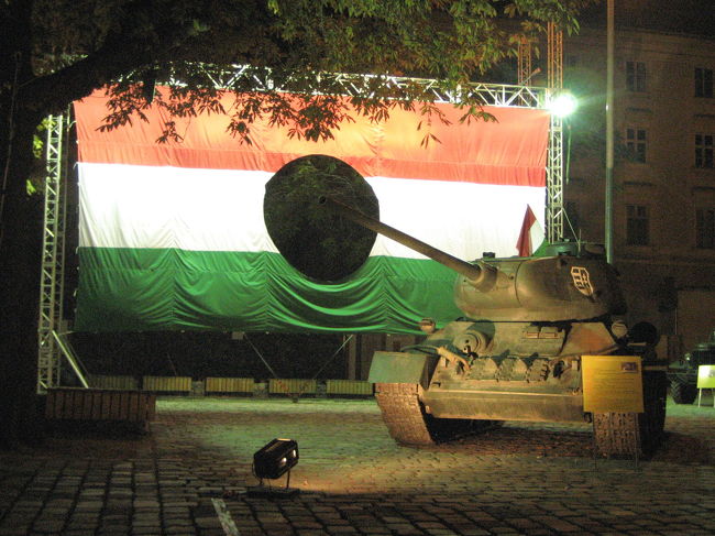 真ん中に穴のあいたハンガリー国旗と戦車<br /><br />「1956年に?ハンガリー動乱?が起こってナジ・イムレが首相になった。政府はソ連から離れて民主的な国を作ろうとしたが、ソ連は装甲車をハンガリーに出動させた。ブダペストでは市街戦が起こって多くの市民が犠牲となり、ナジはソ連軍に連行されて後に処刑される。この事件の後、社会主義者労働党の党首となったカーダールは、ハンガリー国内の反スターリン運動の盛り上がりを止めることはできなかった。ソ連は?ハンガリー動乱?の教訓から、事件以降ハンガリーに対しては黙認することが多くなり、ハンガリーは独自の経済改革を進めていった。」<br />（「旅名人ブックス　ハンガリー“千年王国”への旅」（日経BP社）より