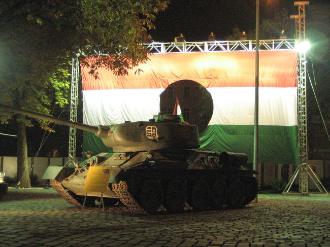 真ん中に穴のあいたハンガリー国旗と戦車<br />アングルを変えて<br /><br />「11月13日、ナジは最後のラジオ演説を行った。「本日未明、ソヴィエト軍が、われわれの合法的・民主的政府を倒すという明白な意図をもって、首都ブダペストに攻撃を開始しました。ハンガリー軍は戦闘中です。政府はもち場についています。私はこの事実を国民と全世界の人々に伝えます」<br />市民は西側諸国の援助や国連の介入を期待していたが、救いの手はさしのべられなかった。民衆の蜂起は、反革命としてソヴィエトの戦車に鎮圧されたのである。」<br />（「図説ブダペスト都市物語」早稲田みか・文（新潮社ふくろうの本）より）<br /><br />軍用トラックなどもありました。<br />ライトに照らされているとはいえ、夜間に撮影するのは限界があります。<br />デアーク広場になら、明日も通りかかるはずなので、明日、また写真を撮ることにしましょう。<br />明日なら、展示も近くで見られるにちがいありません。