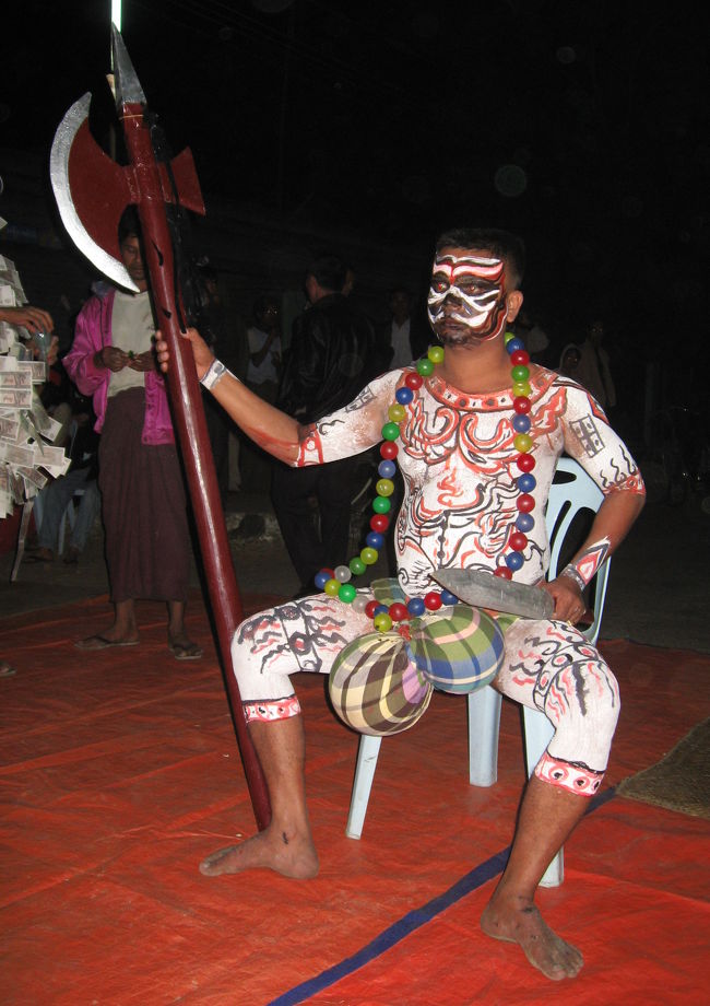 前述の役人さんに最近亡くなった高僧に手向ける踊りの場所に案内して頂いた。<br /><br />写真で見ると、ボディーペインティングに斧と玉を持つ少しコミカルな仮装、に見えるけど、威圧感すごいよ。場を支配している。<br /><br />(僕の英語＋ほんの少しのビルマ語では、文化的背景は分からず)<br /><br />