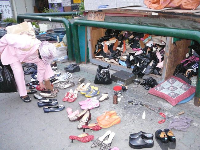 おばさんが靴のためし履き。奥に見えるのが在庫置き場？路上がお店です。<br />どうやって在庫探すのかな（＾＾;