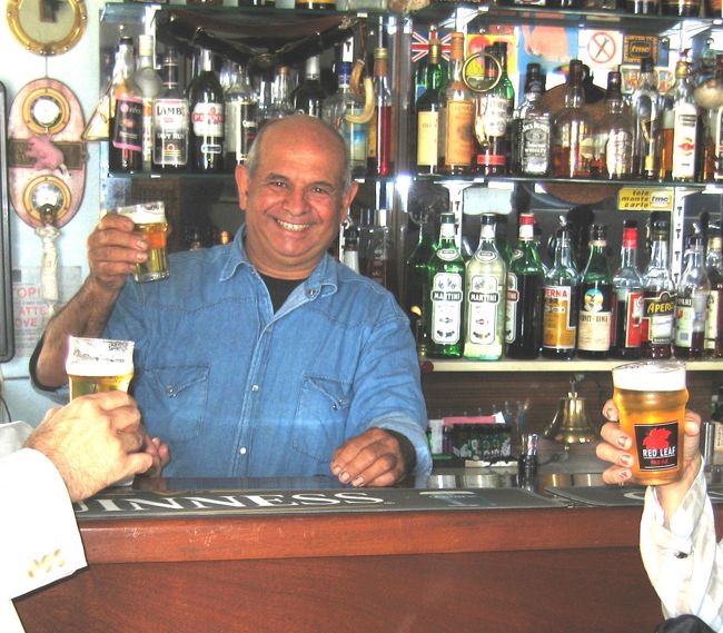 イムジャーの港に映える白亜のバー「グレンイーグルス」。クィネルの「燃える男」に熱く燃えた覚えのある者には、何を置いても立ち寄ってみたいと思うところ。かく言う私もその１人。ガイドの方に朝からおねだり（根回し）した甲斐あって、ちょいと一杯引っ掛ける時間をフェリー乗船までに残して頂いた。胸を高鳴らせて足を踏み入れるや、”背の低い頭の禿げた丸顔のバーテンダー”が”部屋中が明るくなるような、類まれな笑顔”で迎えてくれました。まさしくトニー！！店の雰囲気も、そして、地元の人たちと思しき如何にも頑固そうなオヤジたちも、港の眺めも、全てが小説のそのまんま。感激。トニーと乾杯。今は亡きクィネルの写真にも献杯。忘れえぬ旅の想い出となりました。