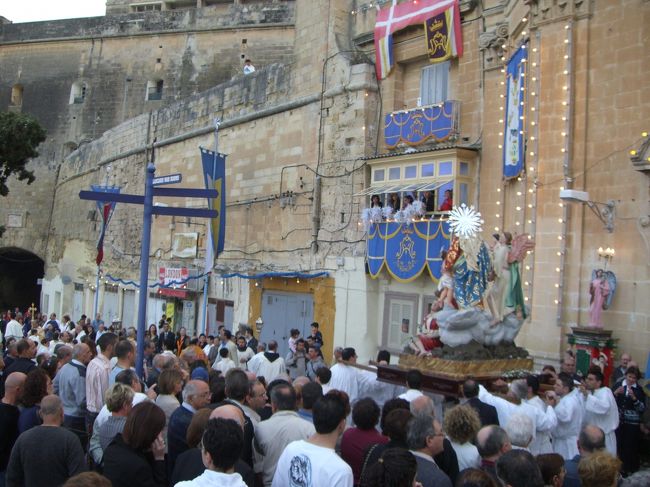 夕刻、ヴァレッタで遭遇した教会のお祭り。日本風に言えば「お神輿」のようなスタイル。教会の鐘は晴れやかに鳴り、階上の窓から女たちは紙ふぶきを降り注ぐ。音楽隊の伴奏と共に通りを練り歩いてました。<br />