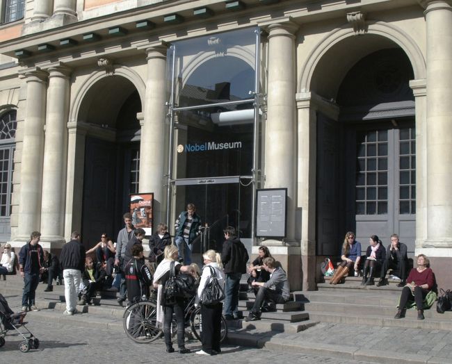 ノーベル賞博物館前の若者たち。<br />中は閑散としていた。この博物館は音と映像を歴代のノーベル賞受賞者の業績を紹介していた。<br />ノーベルさんの記念物を陳列した部屋は興味深かった。<br />なんと言っても、ここの目玉は館内の売店しか売っていないノーベル賞のメダルを模した金色のチョコレートである。貴重な自由時間に、わざわざ、20分もかけて歩き、高い入館料を払って、このチョコレートを買った物好きは私1人だった。因みにメダル一個が10クローネ<br />（200円）だった。