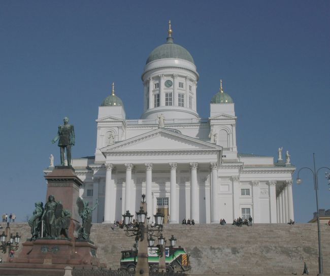 元老院広場に立つロシア皇帝アレキサンドル2世の銅像とヘルシンキ大聖堂。<br />フィンランドは12世紀から凡そ600年間スウェーデンの勢力化にあったが、1709年にスウェーデンはロシアに大敗して、ロシアの勢力化に入り、1809年にはロシアに併合された。4人のロシア皇帝治世下の中でアレキサンドル2世（在位1855-1881)はフィンランド語の使用を認め、善政を敷いた。ロシア革命の混乱の中でフィンランドは独立を達成した、ロシア色が一掃される中で、3人目の皇帝アレキサンドル2世の銅像だけが、そのまま残された。毎年独立記念日の12月6日に、ここで祝典が行われる。<br />明石元二郎は日露戦争当時、北欧を舞台に諜報活動して大活躍し、側面から日露戦争勝利に貢献した。フィンランド独立運動に武器、資金を援助して、ロシア革命の成功、フィンランド独立へ導いた。<br />（「動乱はわが掌中にあり」水木楊より） <br /><br />
