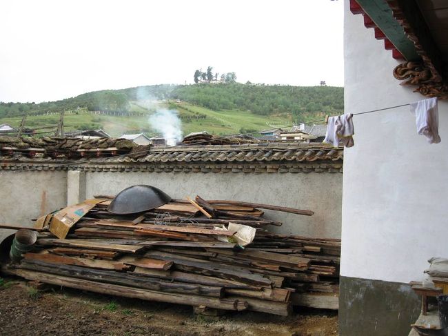 立派な塀で囲まれた屋敷の中の光景です。建材か薪用の木々が積み上げられていました。遠くの山の右手には、東屋風の建物が微かに見えます。