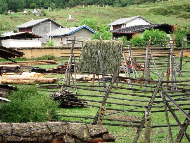 ２階の部屋から眺めた村の光景です。干し台に少しばかりの農作物が架けられ、作業のチェーンソーの音が続いていました。