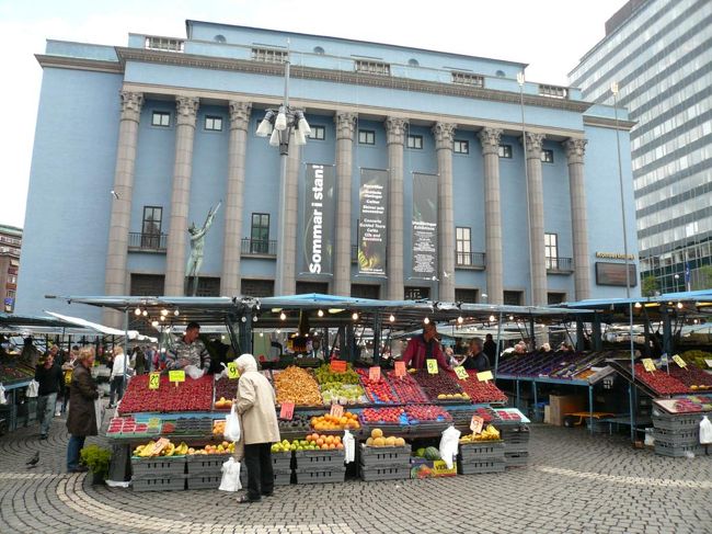 15時ごろ、雨が上がった。 <br /><br />地下鉄でT-Centalen駅からÖstermalmstorg駅まで行き、何件かショップを見たり、 音楽博物館 Musikmuseetを見学したりしながらHötorget方面へ歩いていった。 ショップでは特に欲しい物もなかったので何も買わず。 <br /><br />写真はHötorgetの市場。  後ろの建物はストックホルム・コンサートハウス Stockholms Konserthus。 