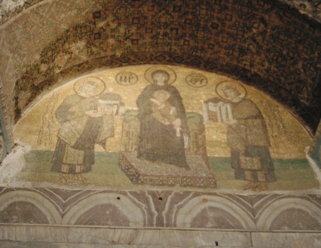 次に近くのアヤ・ソフィアに案内される。<br />写真は拝廊入口のイコン。中央はマリア、右はマリアにコンスタンチノーブルを捧げるコンスタンティヌス帝、左はマリアにアヤソフィアを捧げるユスティアヌス帝。<br />アヤソフィアはAD537年にローマ皇帝ユスティニアヌスが再建した大聖堂である。900年間、キリスト教の大聖堂として機能してきたが、1453年にオスマン・トルコに破れ、ビザンチン帝国は滅亡する。コンスタンチノーブルはイスタンブールと改名され、大聖堂内のイコンは漆喰で塗り込まれ、イスラム教のモスクとして500年間使用されてきた。1923年のトルコ共和国誕生後、アヤソフィアは博物館に生まれ変わった。塗り込められたイコンは漆喰をはがし、姿を見せつつある。現在、欧米のキリスト教徒の間で、ギリシャ正教の総本山に戻す運動があるようだ。