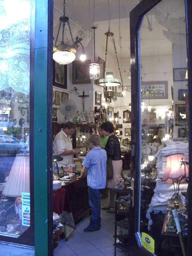 ☆骨董屋通りにて<br /><br />ＦＡＬＫ　ＭＩＫＵＳＡ通りに多くある骨董屋を覗いて歩きました。と言っても、物色するのは家内ばかりですが。<br /><br />この店では、年の頃なら小学校高学年ぐらいでしょうか、店主の子供が健気に店を手伝っておりました。一端の骨董商の顔つきで、お客に対応するその姿は微笑ましくもあり、たくましくもありました。こうやって代々商売が継承されて来て、そして、継承されていくのでしょう。客との値段交渉となると、さすがに親父さんの出番となっていました。<br /><br />ちなみに、数少ない経験からですからアテにはなりませんが、全体的に値段に対しては脇が固いように感じました。中央市場のちょっとした土産物でも、真顔でかたくなに拒まれることが多かったです。あまりにも真顔で答えてくれるので、「ん？値切ろうとするオレって、もしかして非常識なのかしらん？」と気がひけてしまうほど。もしもこれが作戦だとしたら、役者やのぉ、ハンガリー人！！<br />