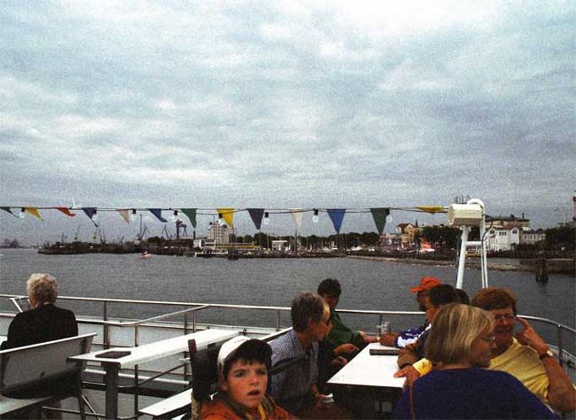 港内巡回する観光船に乗る。背景は以前からある造船所付近。<br /><br />港全体は落ちぶれた雰囲気で、波止場に係留して荷役する船は皆無。波止場には曲がった形状の（統一した形状の商品ではない）雑木とくず鉄が積み上げられたまま。<br />この一帯は北欧系の名前をつけ新しいく改装された造船所だ。恐らくドイツ統一後に身売りしたのだろう。ただ建造中の船は小さな客船１隻だけでさびしそうで、今日は木曜日なのに人影は見えず、休日？。大国の統一は10年経ってもまだひずみがあって個人も会社も大変なんだと実感。