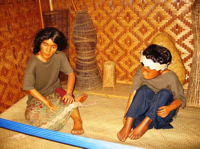 家の中で寛ぐ兄弟を表現した蝋人形のようです。壁などは、椰子の葉などを使った編み物細工のようです。