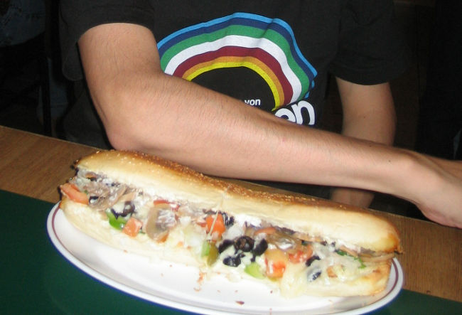 【ごはん難民になる】<br />Kマートのあとは、夕食を目指してグアム一番の繁華街、DFSギャラリア周辺へ。<br />アウトリガーホテルを中心とするこのエリアは、きらびやかなネオンに彩られて華やかな雰囲気。<br />到着そうそうから天気が悪く、なんだか暗〜く見えたグアムの街が、ここへ来てようやく「おぉ〜、リゾート！」という感じに見えるようになりました。<br /><br />アウトリガーのトイレを拝借して、気持ちよ〜くオムツ替えを済ませた頃には既に夜7時30分すぎ。<br />息子の普段の夕食時間はとっくに過ぎています。<br />この日は特に行きたい店を決めていなかったので、「早くどこかでごはんを食べさせなきゃ！」とあせりながらガイドブックをチェック。<br />時間もないから、すぐ近くの「The Plaza」というショッピングモールのフードコートで軽く済ませよう！ということに。<br /><br />しかし、行ってみてビックリ。<br />このフードコート、恐ろしく暗いんです！！<br />ショッピングモールはオシャレな雰囲気なのに、どうして〜?!<br />さすがにグアム最初の夜の食事を、こんなところで食べるのはどうかということで、パスしました。<br /><br />じゃあ次は、同じモール内のイタリア料理店「ヴィタリーズ」を目指すことに。<br />しかし、探せど探せど見当たらない！<br />このビル、坂の途中にあって階数がよく分からない上に、改装中の部分があったりして迷路のように入り組んでいるんです。<br />どんどん時間は過ぎ、息子の機嫌も悪くなるいっぽう。。<br />あせればあせるほど空回りしてしまう私たちでした。<br /><br />なんとか店を見つけ、料理をオーダー。<br />チキンのピザのスモールサイズと、マッシュルームたっぷりのサンドイッチ、そしてドリンク。<br />料理はどちらも想像通りのビッグサイズです。<br />サンドイッチは半分のこしてテイクアウトし、翌日の朝ご飯にしました。<br /><br />息子は持参したレトルト離乳食とベビーダノン、あとはピザのはしっこやサンドイッチのパンをつまみ食い。<br />ハラが減っていたのか、美味しかったのか、すごい勢いでむさぼり食っていました。。<br /><br /><br />＊写真／足のサイズ28cmのダンナのひじと同じくらいビッグなサンドイッチ。料理はどちらもグッチョイ！店内は半分以上が地元の人。大いに賑わっていたので、息子が騒いでも気になりませんでした。