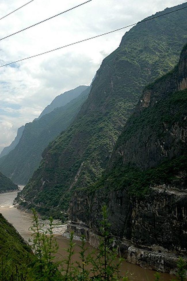 迪慶チベット族自治州側から見た金沙江下流方向と麗江市側の虎跳峡絶壁。<br />麗江市側の遊歩道がその岩山の下の方に付いているのが見えています。<br /><br />この部分の金沙江は麗江市側の玉龍雪山（５５９６ｍ）や迪慶チベット族自治州側の哈巴雪山（５３９６ｍ）の間を通るので、虎跳峡の川から尾根の高低差は３０００ｍ以上になる部分もあるのだそう。<br /><br /><br />画像左奥から岩山が少し突き出している部分に迪慶チベット族自治州側の駐車場があって、そこから虎跳峡の流れ間近まで下りて行けるんですが…、<br />