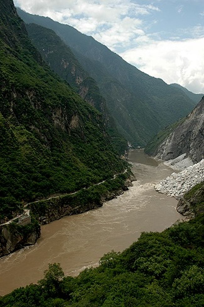 虎跳峡が一番狭まって虎跳石と名が付いた場所へ下りて行く途中、迪慶チベット族自治州側から見た景色。<br /><br />これは金沙江の上流方向。<br /><br />２００３年に世界遺産の自然遺産になった雲南保護地域の三江併流群の三江とは、金沙江（長江上流の名）、瀾滄江（メコン川上流の名）、怒江（サルウィン川の上流の名）流域の一帯ということで、この金沙江沿いの風景も含まれているんだそうです。<br /><br /><br />麗江市側の山肌に遊歩道があるのがくっきり見える。<br />そこを歩いている人々の姿も写っているんですが、この画像だと見えないですね。<br /><br />